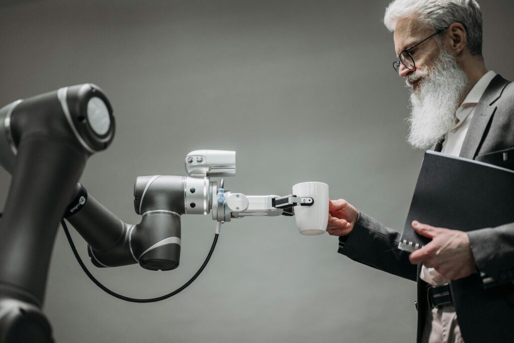 pexels-photo-8439093-8439093 An elderly man receives a cup from a robotic arm in a modern office setting.